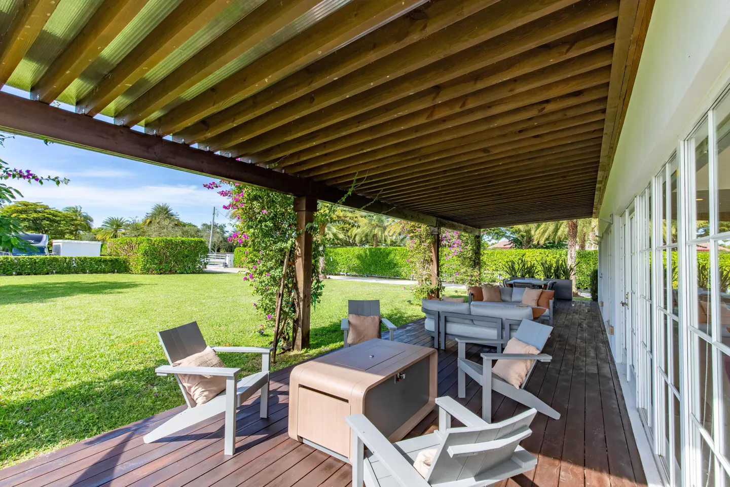 Covered patio with wooden pergola, gray furniture, and a green lawn in the background.