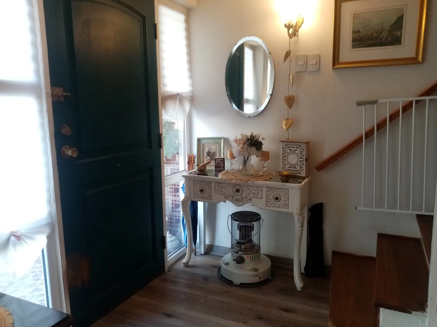 Entryway with a dark green door, white console table with decor, oval mirror, and stairs with a white safety gate.