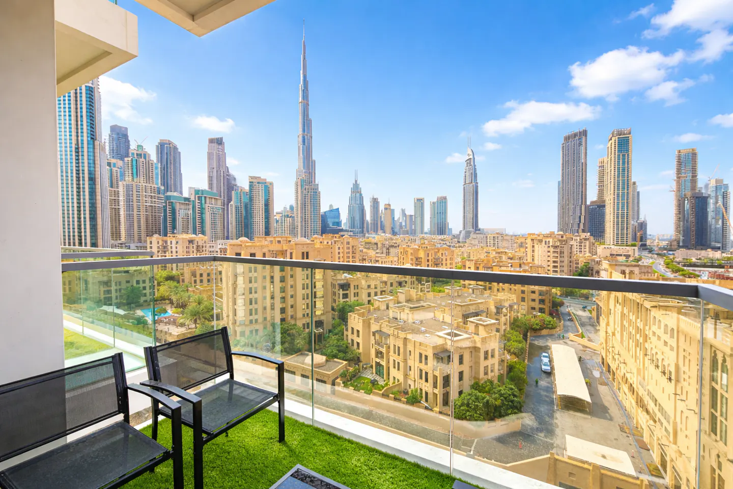 Balcony view of Dubai skyline. Two black chairs sit on green turf. The Burj Khalifa tower is visible in the background.