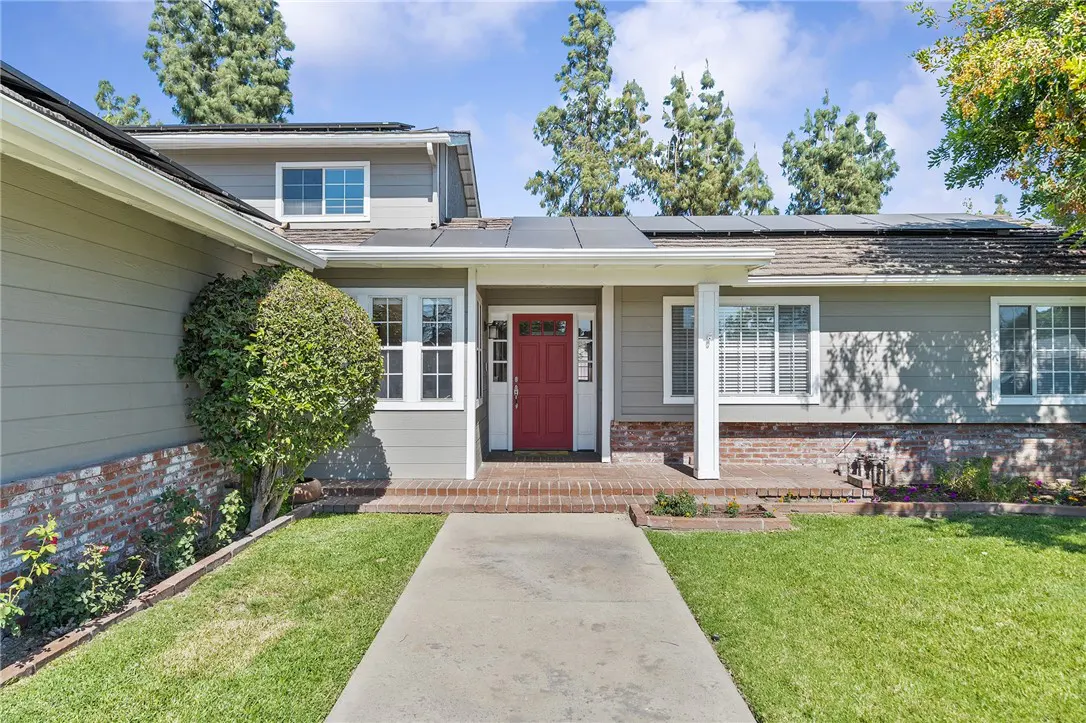Exterior of a one-story house with gray siding, white trim, and a red front door. A concrete walkway leads to the entrance.