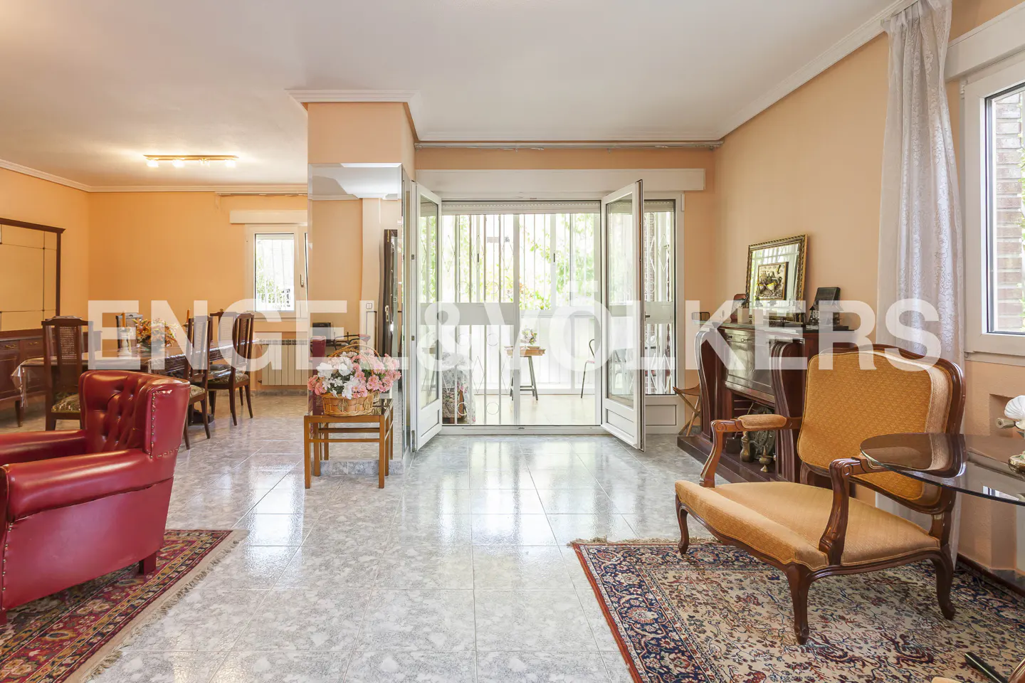 Spacious living room with peach walls, tile floors, a red leather armchair, and an orange upholstered accent chair.