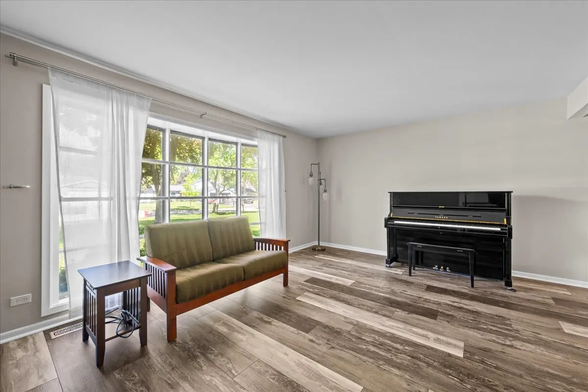Living room with wood-look floors, a green loveseat, a small side table, a floor lamp, and a black upright piano.
