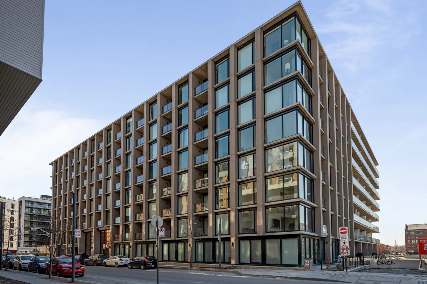 Exterior view of a modern, multi-story apartment building with balconies and large windows on a city street.