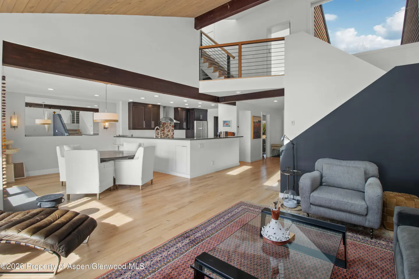Open-concept living space with hardwood floors, dining table, kitchen, and gray accent wall. A staircase leads to a loft area.