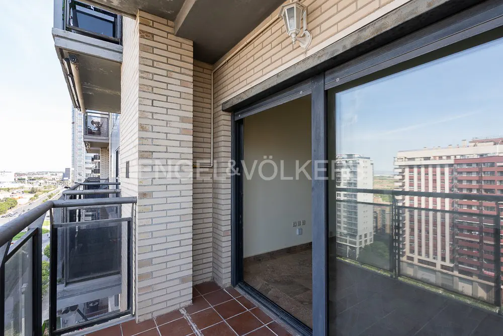 Balcony view with brick walls, brown tile floor, and sliding glass doors. City buildings are visible in the background.