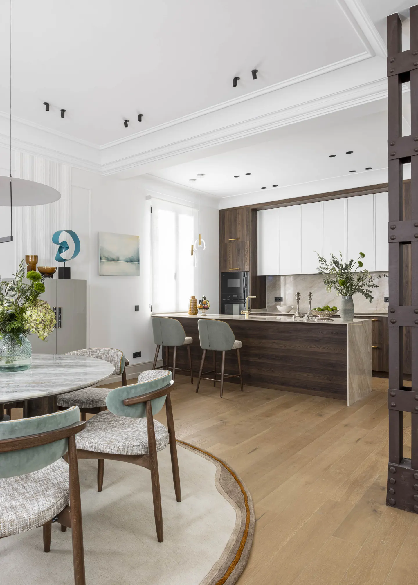 Open-concept kitchen and dining area with light wood floors, marble table, and island. White cabinets contrast with dark wood accents.