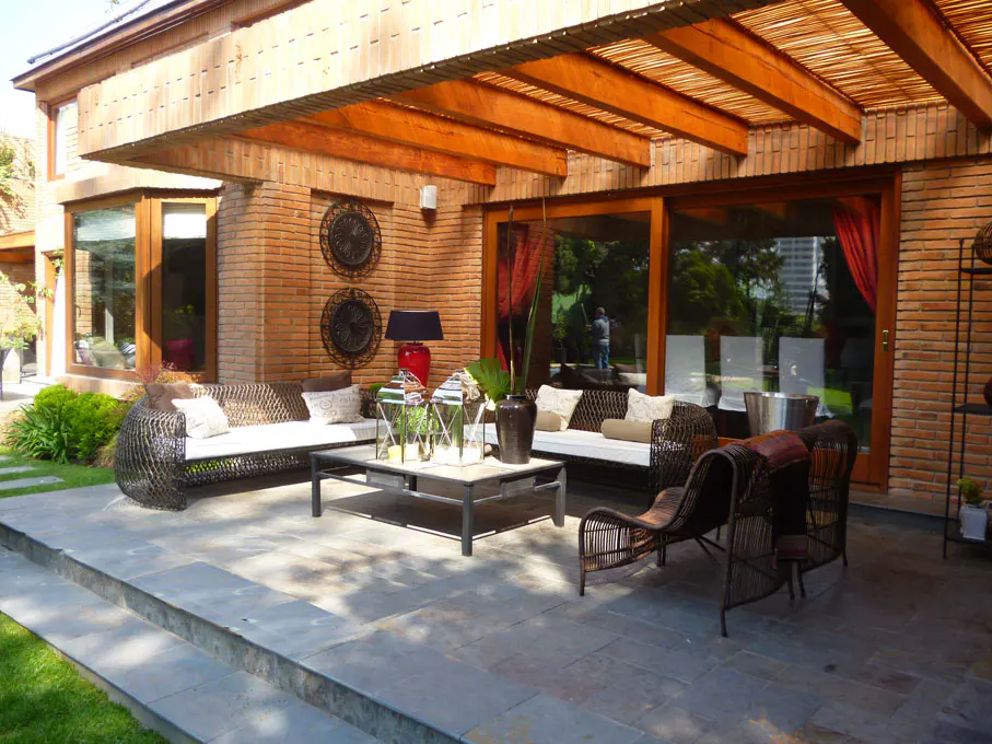 Outdoor patio with wicker furniture, stone flooring, and brick walls. A wooden pergola covers the seating area.