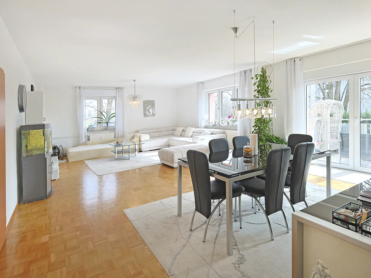 Bright open-plan living room with hardwood floors, a white sectional sofa, and a dining area with a glass table and chairs.