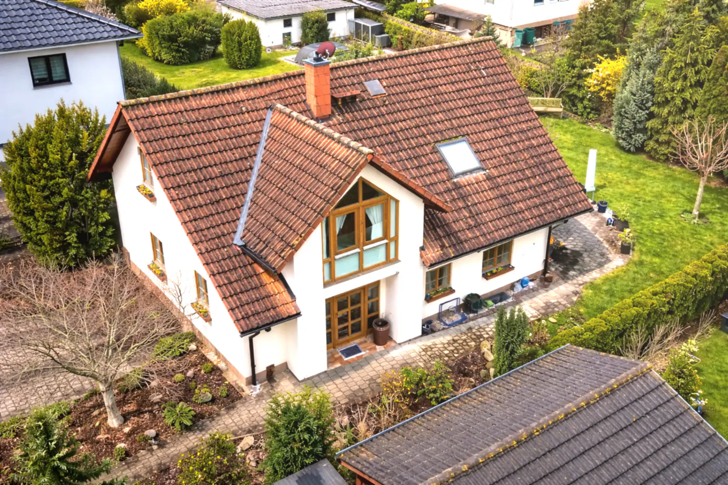 Aerial view of a two-story white house with a brown tile roof, surrounded by a green lawn and trees.