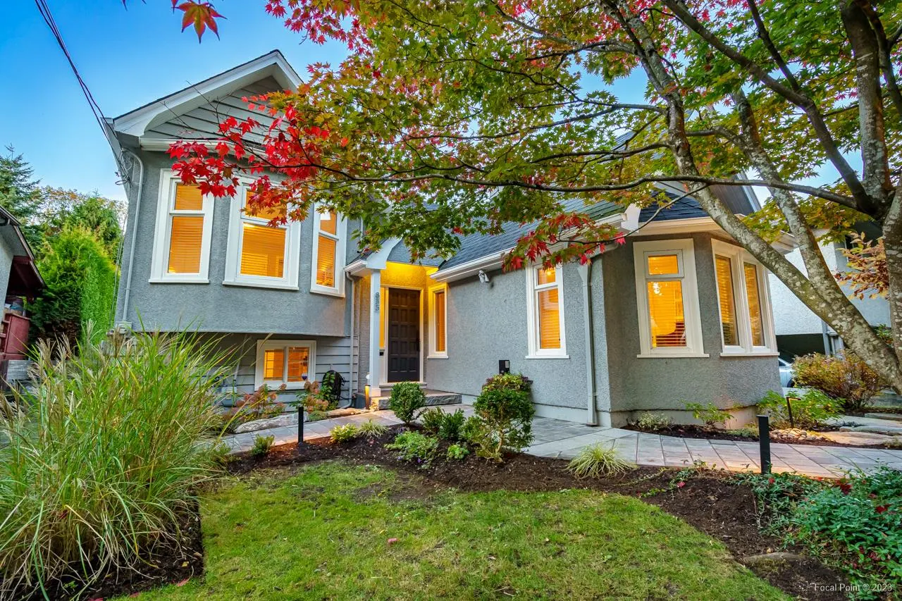 Gray two-story house with white trim, black door, and autumn foliage. Lawn and garden in front.