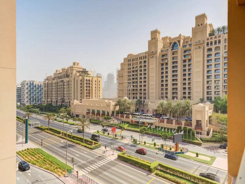 View from a high-rise of a wide street with cars, palm trees, and large beige buildings in Dubai.