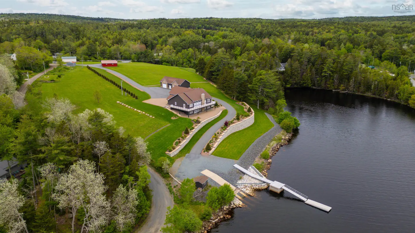 Aerial view of a dark gray house with a dock on a lake, surrounded by green trees and grass.