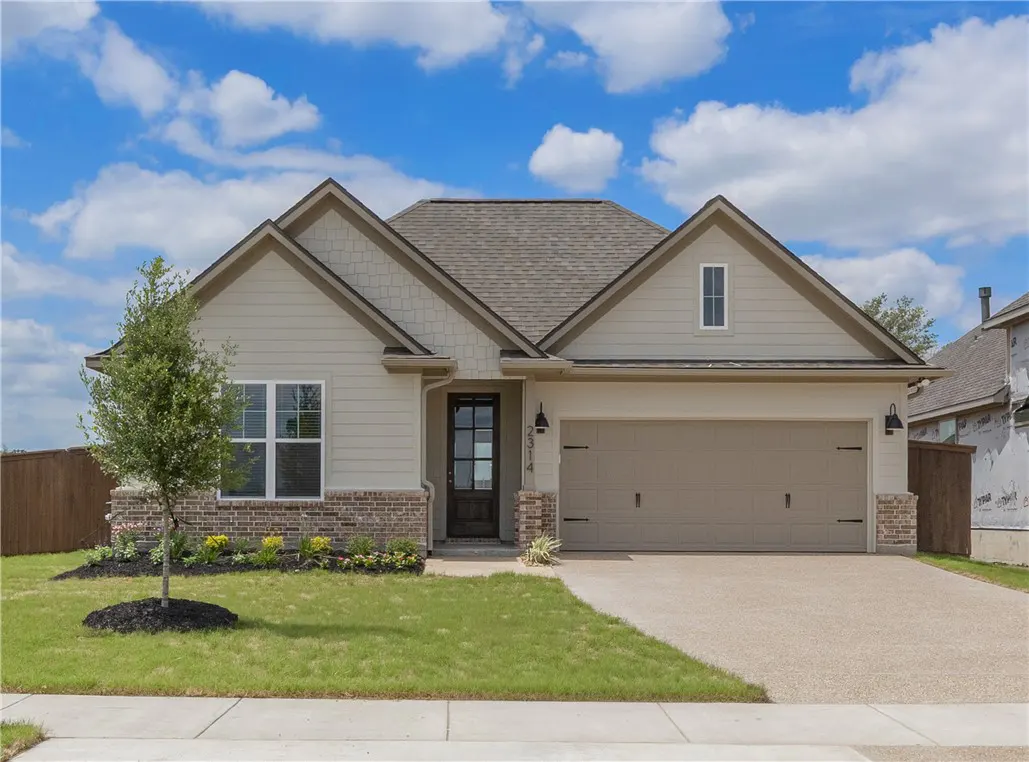A single-story house with a beige exterior, a brown roof, and a two-car garage on a sunny day.