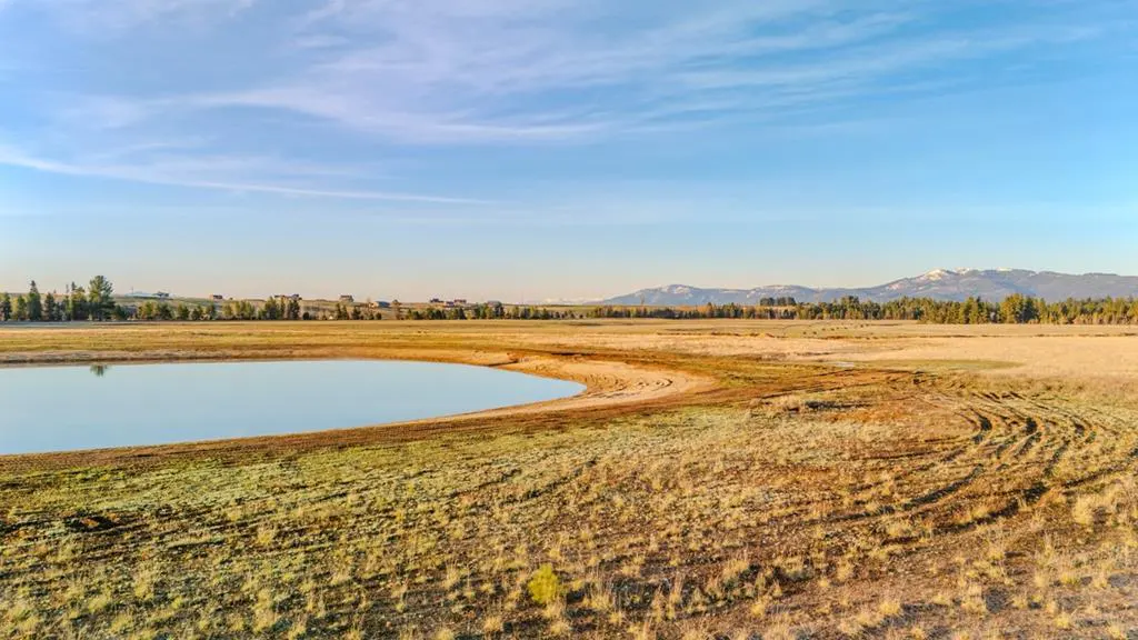 Scenic view of a blue pond surrounded by golden fields under a clear sky, with distant mountains.
