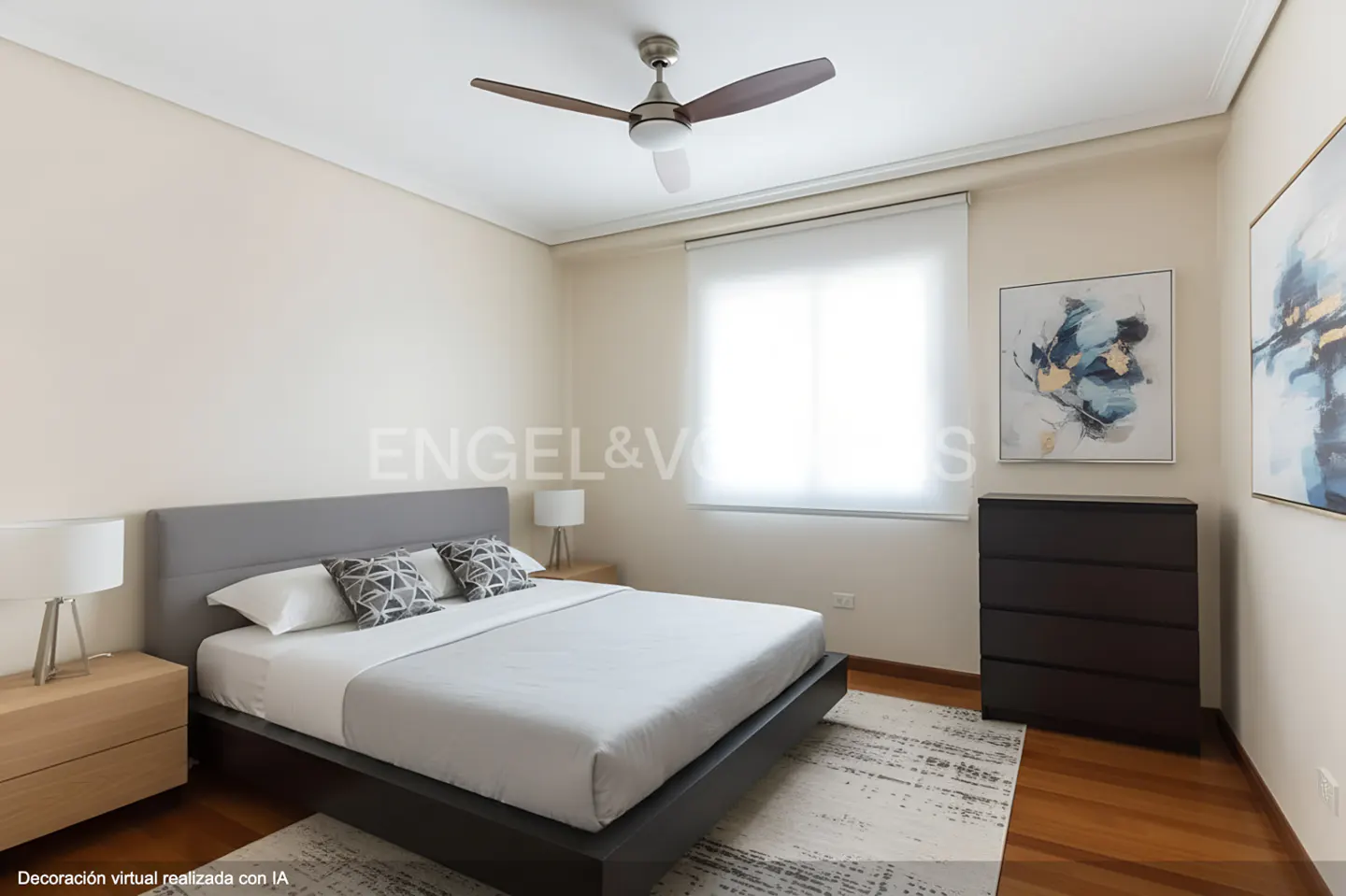Bedroom with a gray bed, white linens, and geometric pillows. A ceiling fan, dresser, and abstract art complete the room.