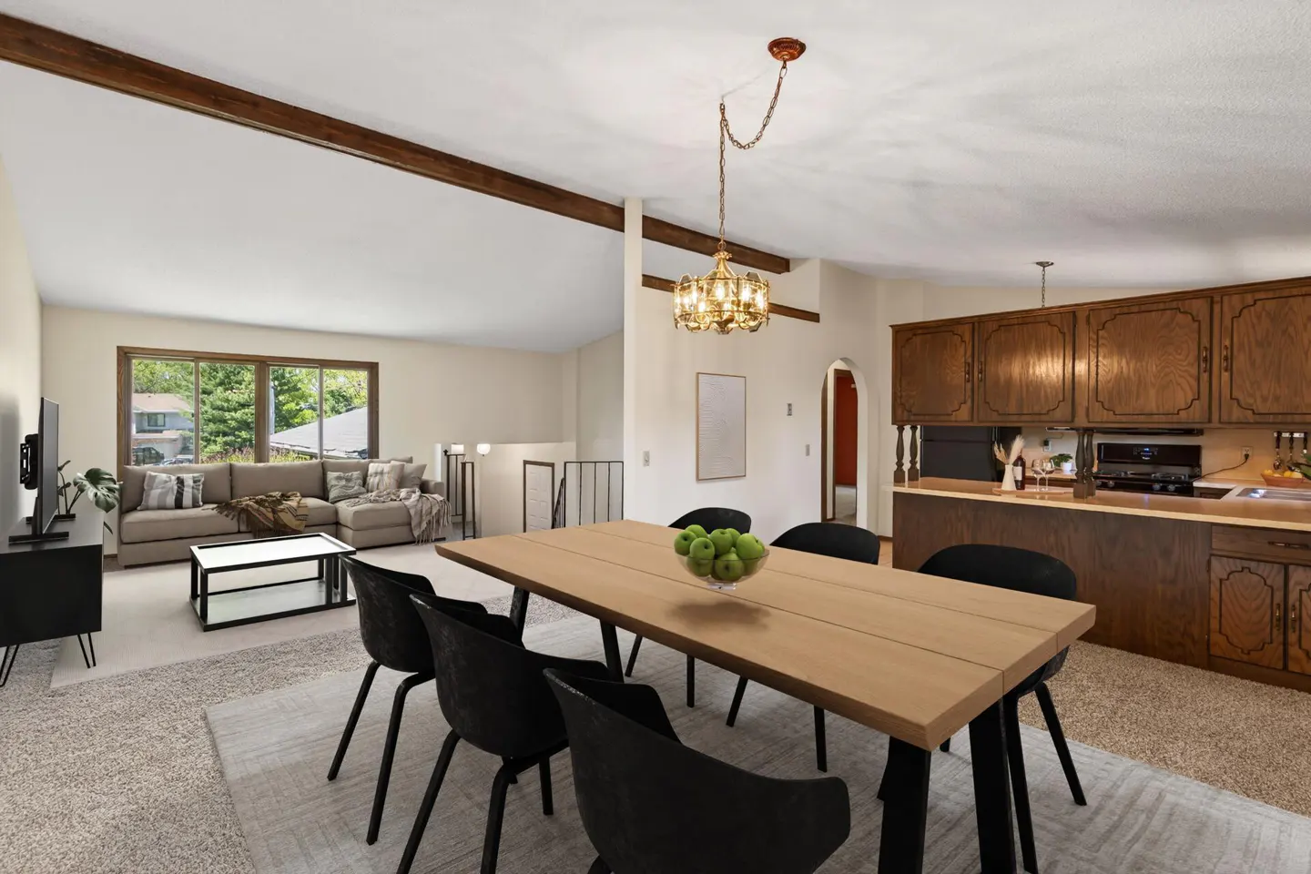 A bright, open-concept living and dining area with a wooden table, black chairs, and a view of the living room and kitchen.