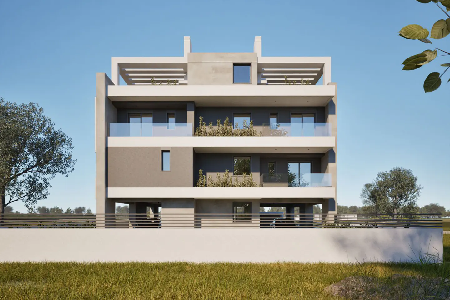 Three-story gray apartment building with balconies and a white fence, set against a blue sky and green grass.
