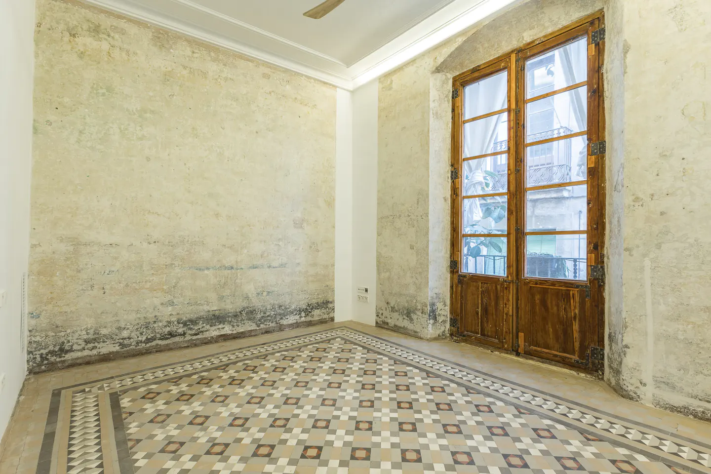 Empty room with patterned tile floor, textured walls, and a large wooden double door leading to a balcony.