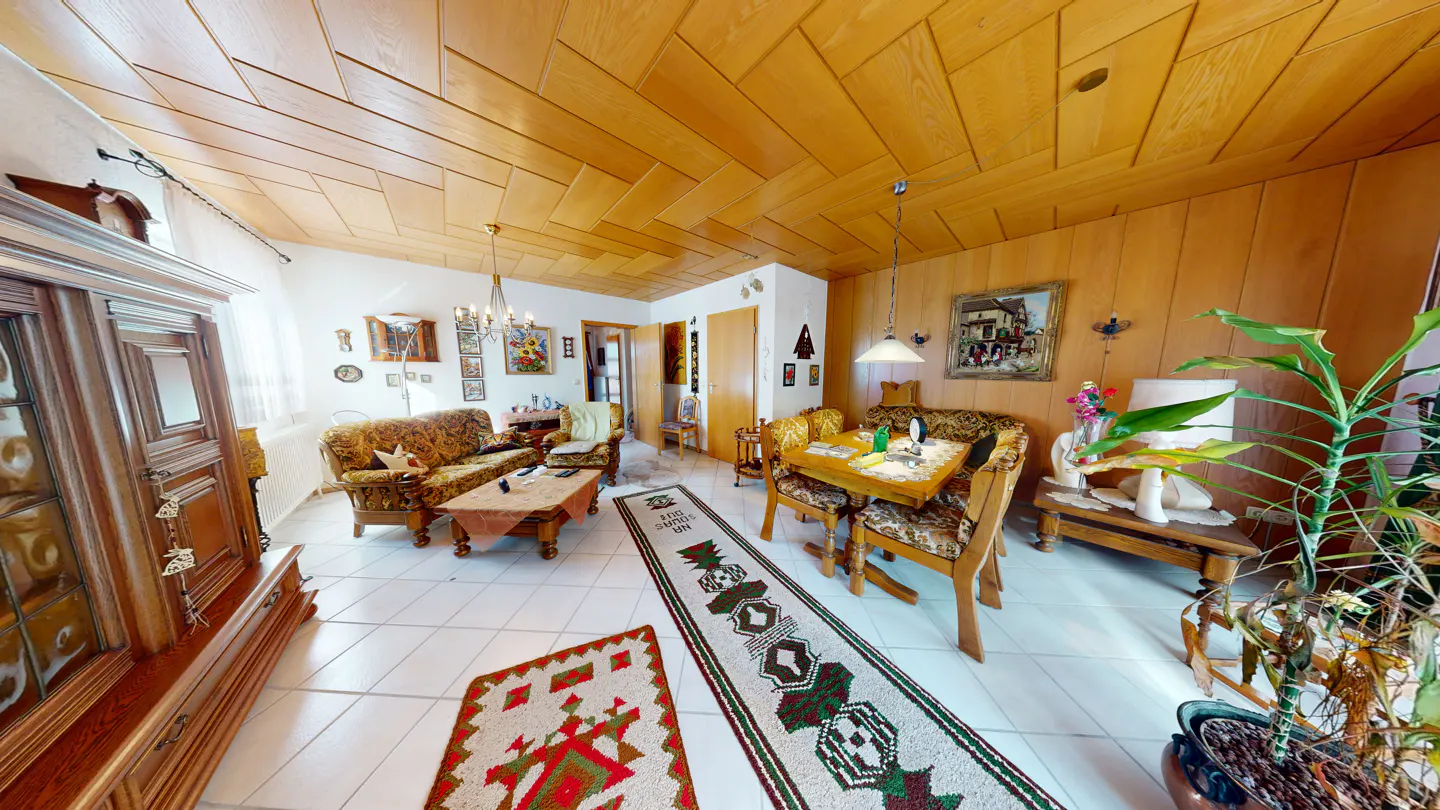 A living room with wood paneled walls and ceiling, patterned sofas, and a dining table.
