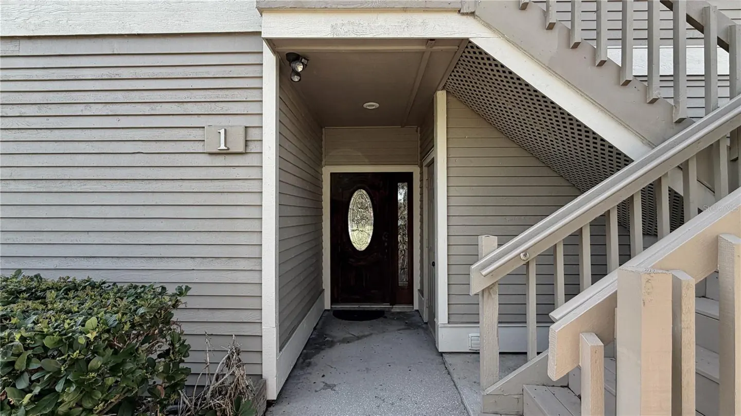Exterior view of a gray, two-story condo with a dark wood front door with oval glass. Stairs lead to the second floor. Unit number 1 is visible.