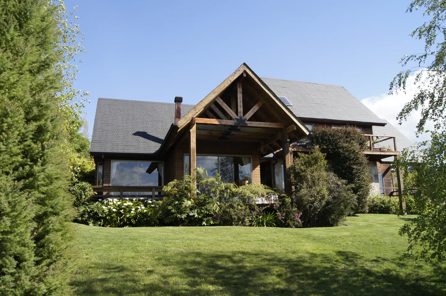 A two-story wood house with a gray roof and a green lawn on a sunny day.