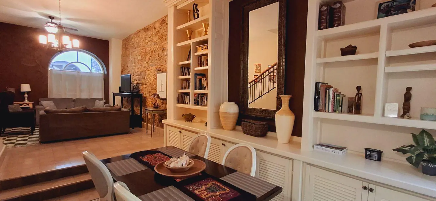 A living room with a dining table, brown sofa, stone wall, and white built-in shelves with books and decor.