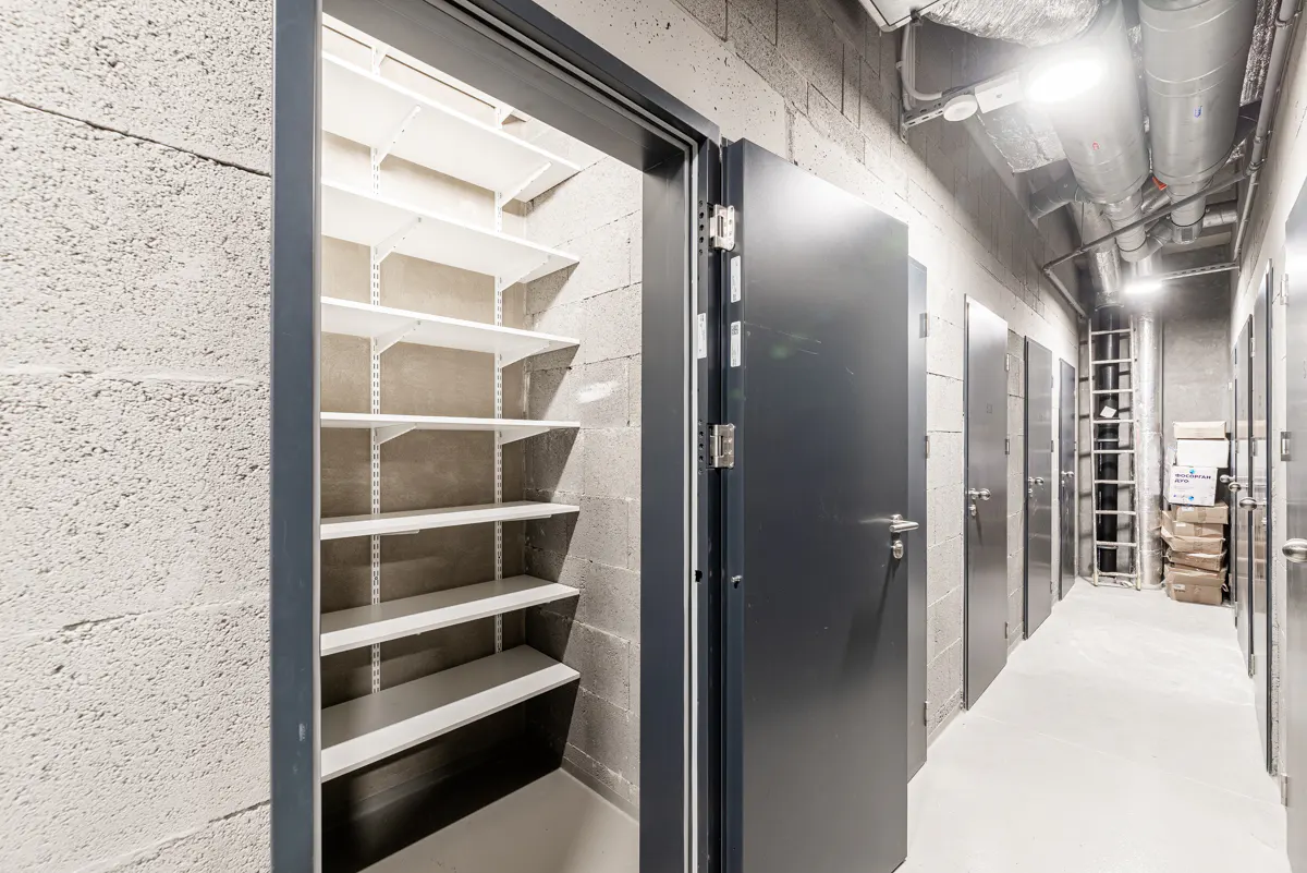 Storage unit hallway with open door to shelving. Gray cinder block walls, gray doors, and white shelves.
