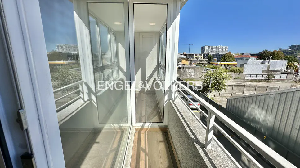 Balcony view with white railings, glass doors, and a glimpse of the city skyline under a clear blue sky.
