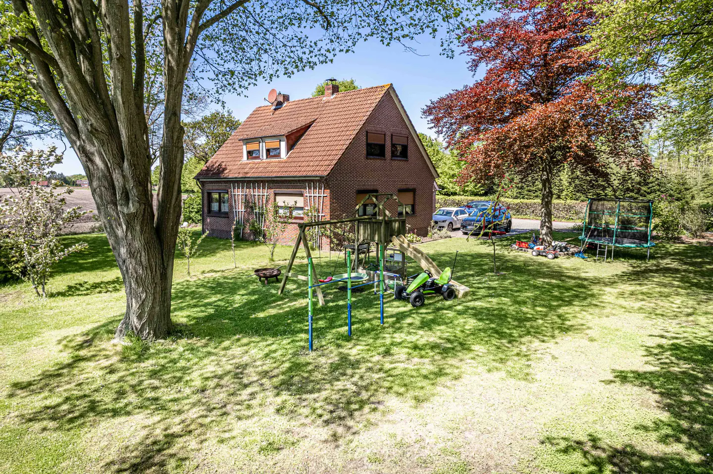 Two-story brick house with a red tile roof, a swing set, and a trampoline in the yard.