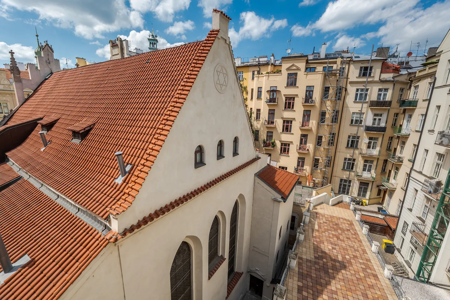 Aerial view of the Old New Synagogue in Prague, featuring a red-tiled roof, white walls with arched windows, and a Star of David emblem.