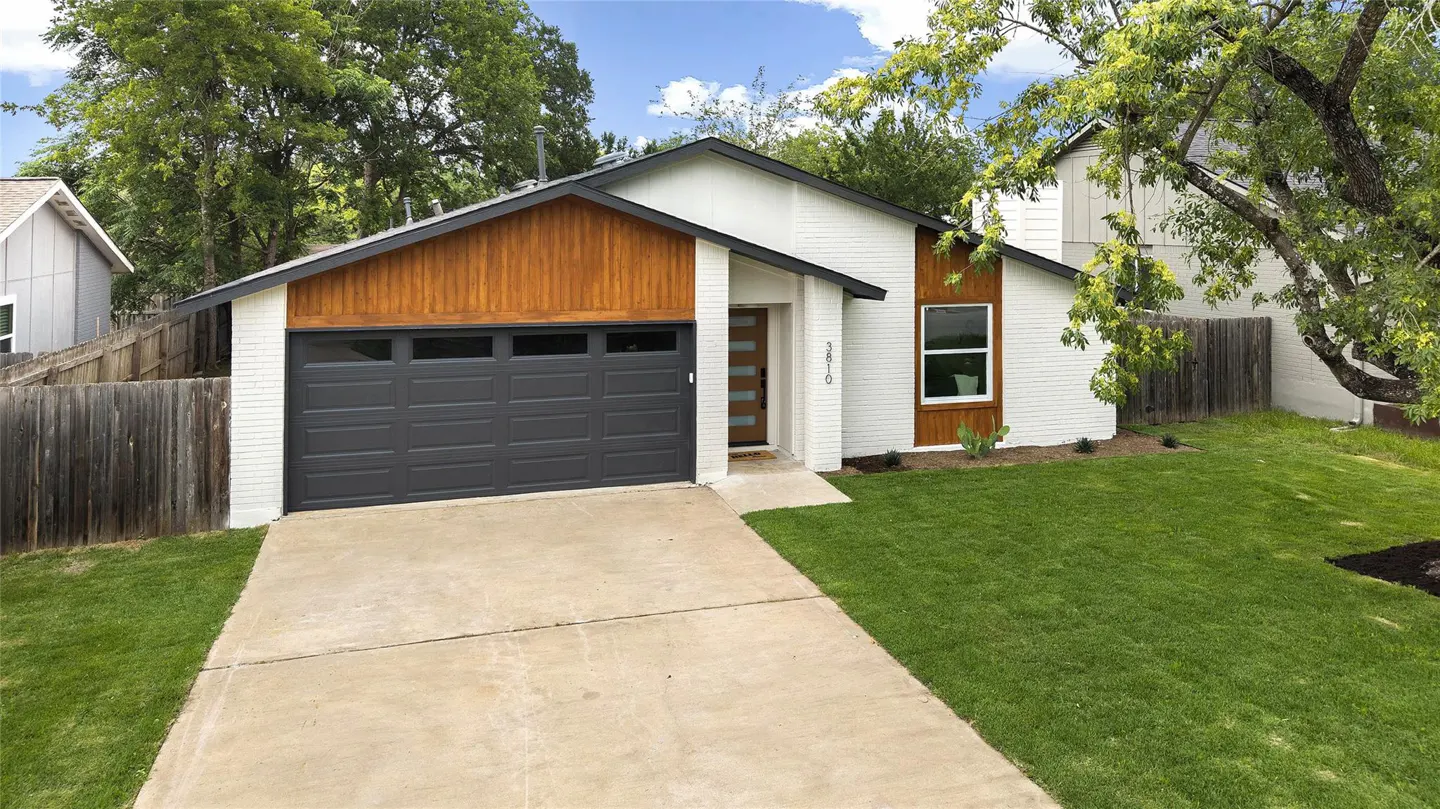 A white brick house with a gray garage door, wood accents, and a green lawn on a sunny day.