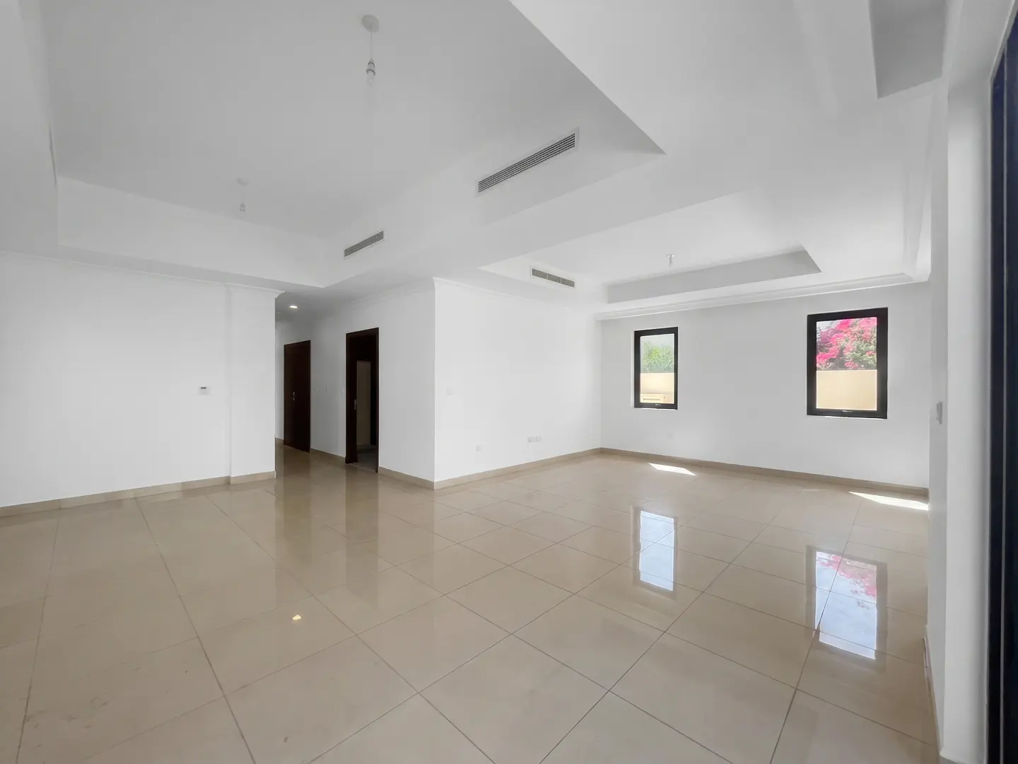 An empty room with white walls, beige tile floors, and two windows.