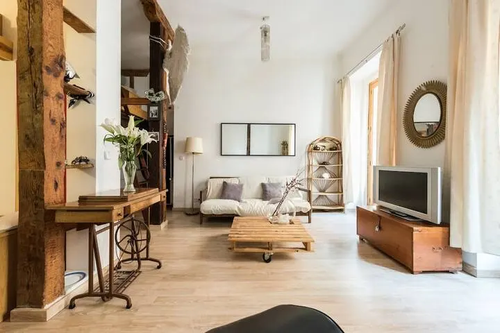 Bright living room with a white sofa, wooden pallet coffee table, vintage sewing machine desk, and a TV on a wooden chest.