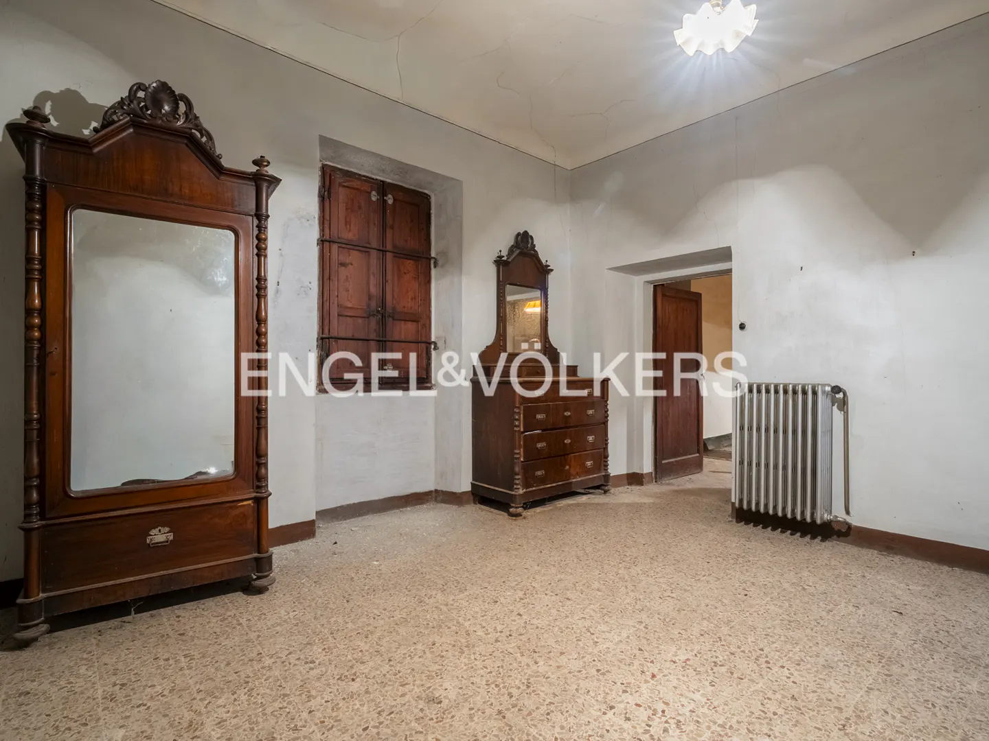 A room with a wardrobe, dresser, radiator, and window with closed shutters.