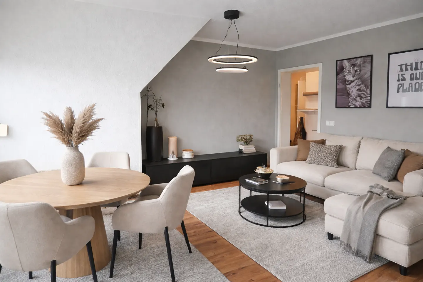A modern living room with a round wooden table, beige chairs, a white sofa, and a black coffee table on a gray rug.