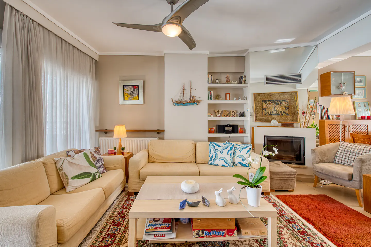 Living room with beige sofas, a light wood coffee table, and a red patterned rug. A fireplace and built-in shelves add character.