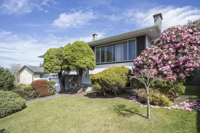 Exterior view of a two-story house with a green lawn, trees, and a large pink flowering bush.