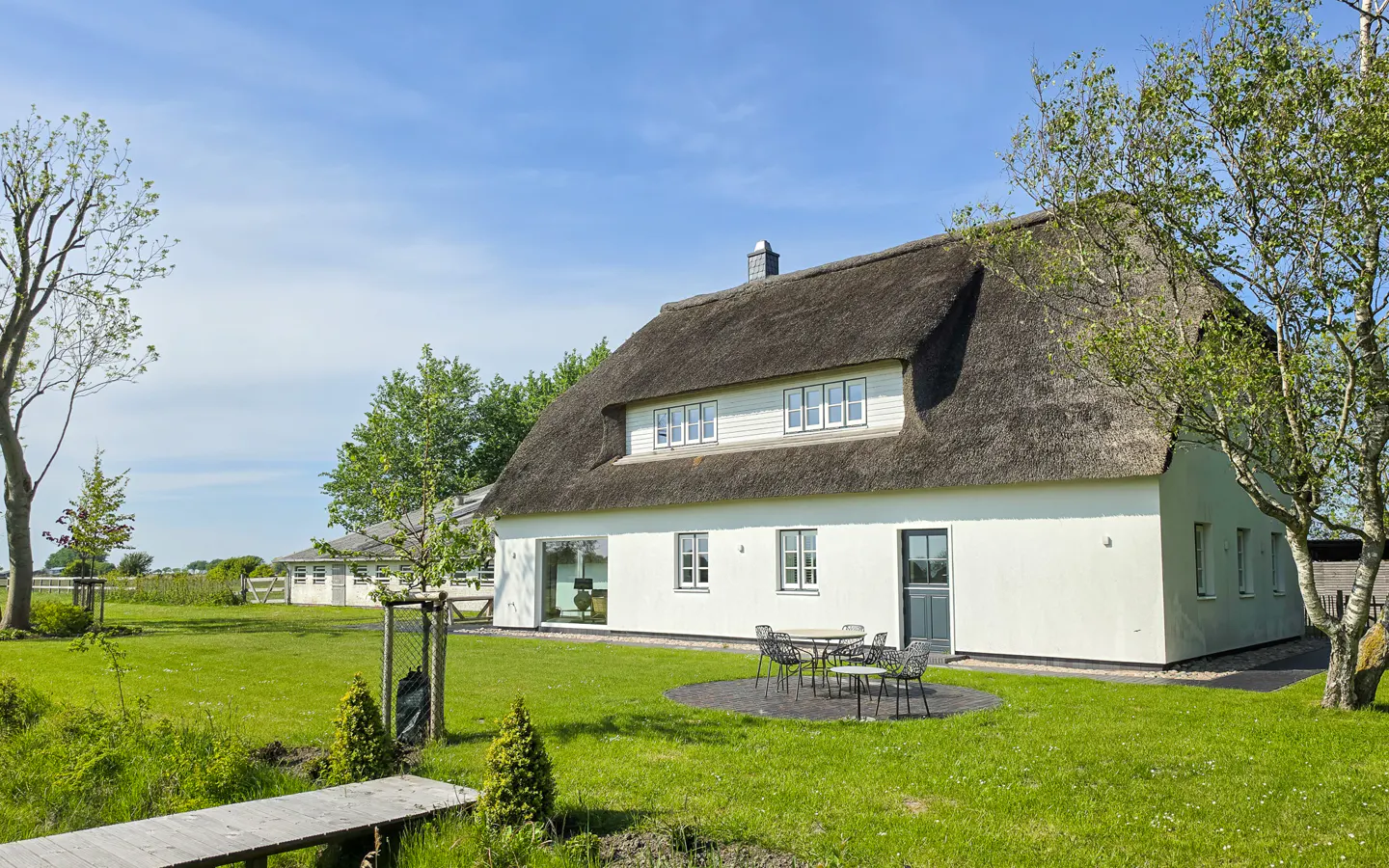 Exterior of a white house with a thatched roof, green lawn, and outdoor seating area.