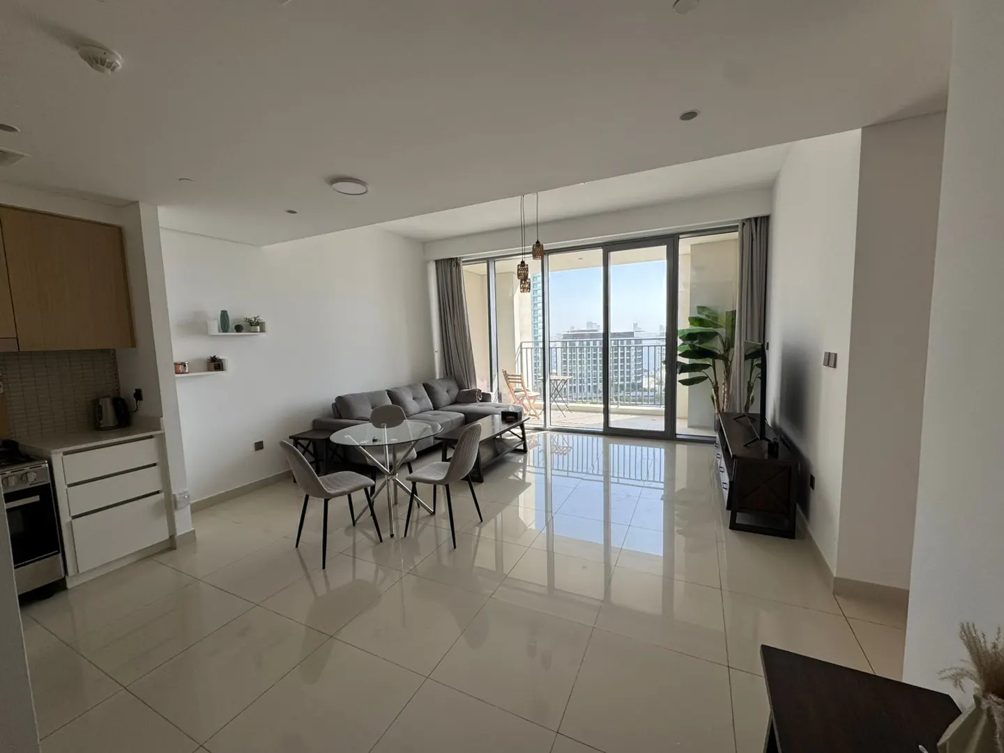 Bright, modern apartment interior with gray sectional sofa, round table with chairs, and balcony with city view.