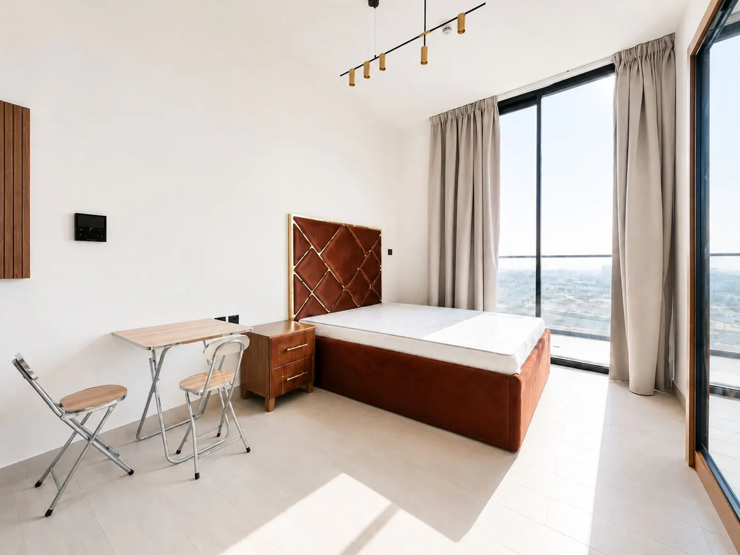 Bright bedroom with a brown bed, nightstand, folding table and chairs. Large windows with curtains offer a scenic view.