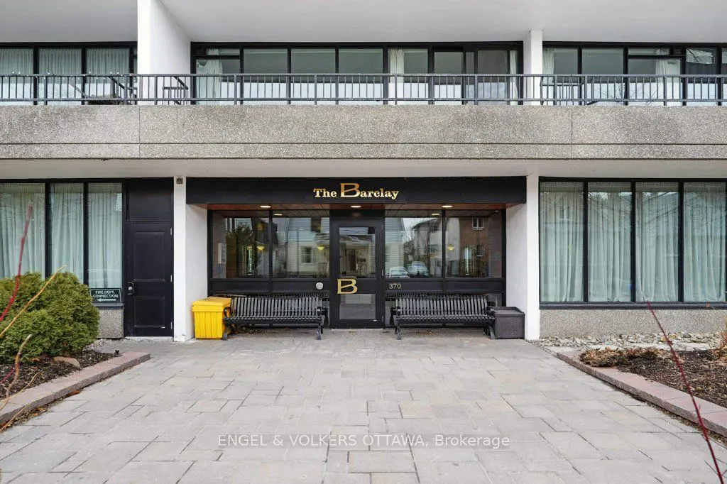 Exterior of The Barclay building with black benches, a yellow bin, and a stone walkway.