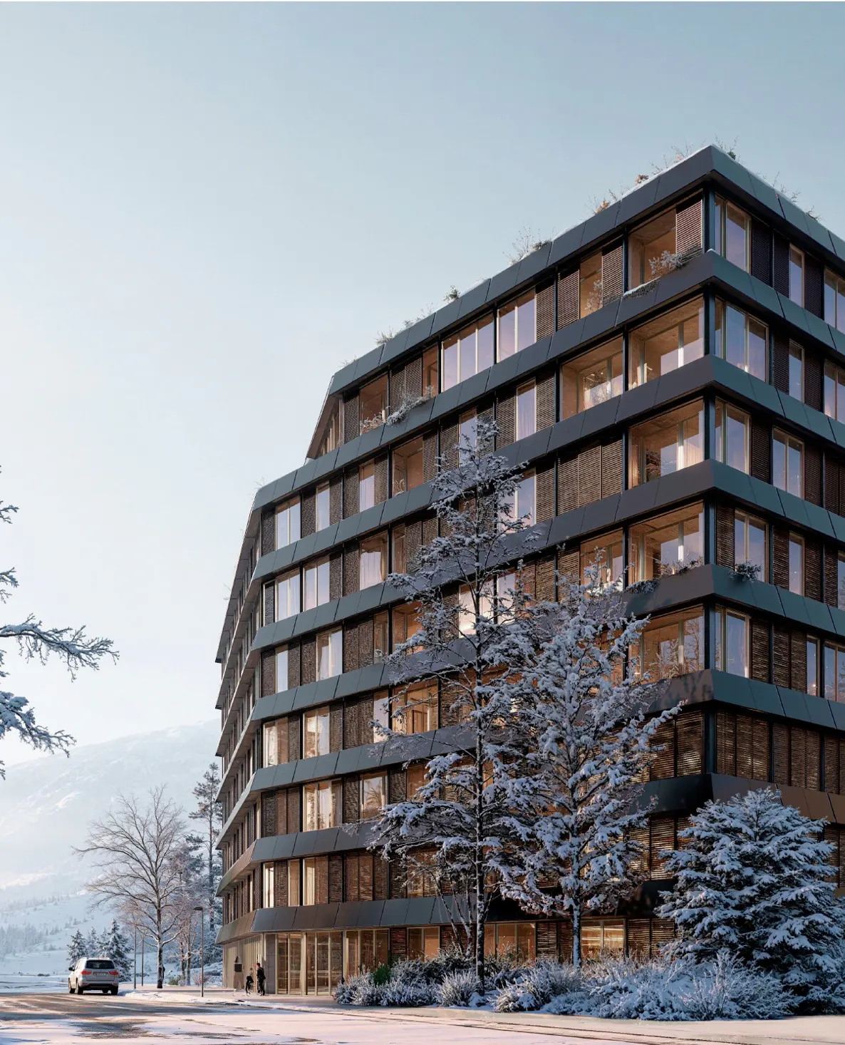 Modern, multi-story apartment building with large windows, surrounded by snow-covered trees and ground. Blue sky in the background.