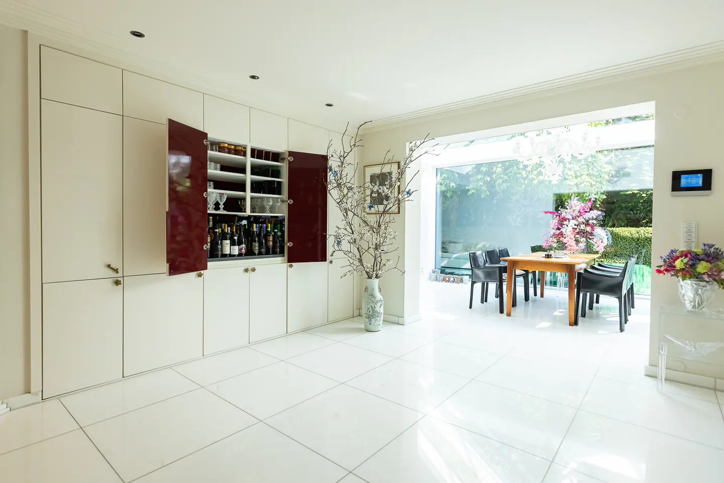 Bright, modern dining room with white tile floors, built-in cabinets, and a view of the garden through a large glass wall.