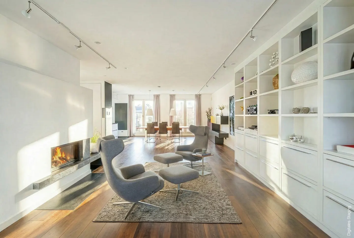 Bright, open-concept living space with hardwood floors, a fireplace, and two gray chairs with ottomans. A white bookcase lines the wall.