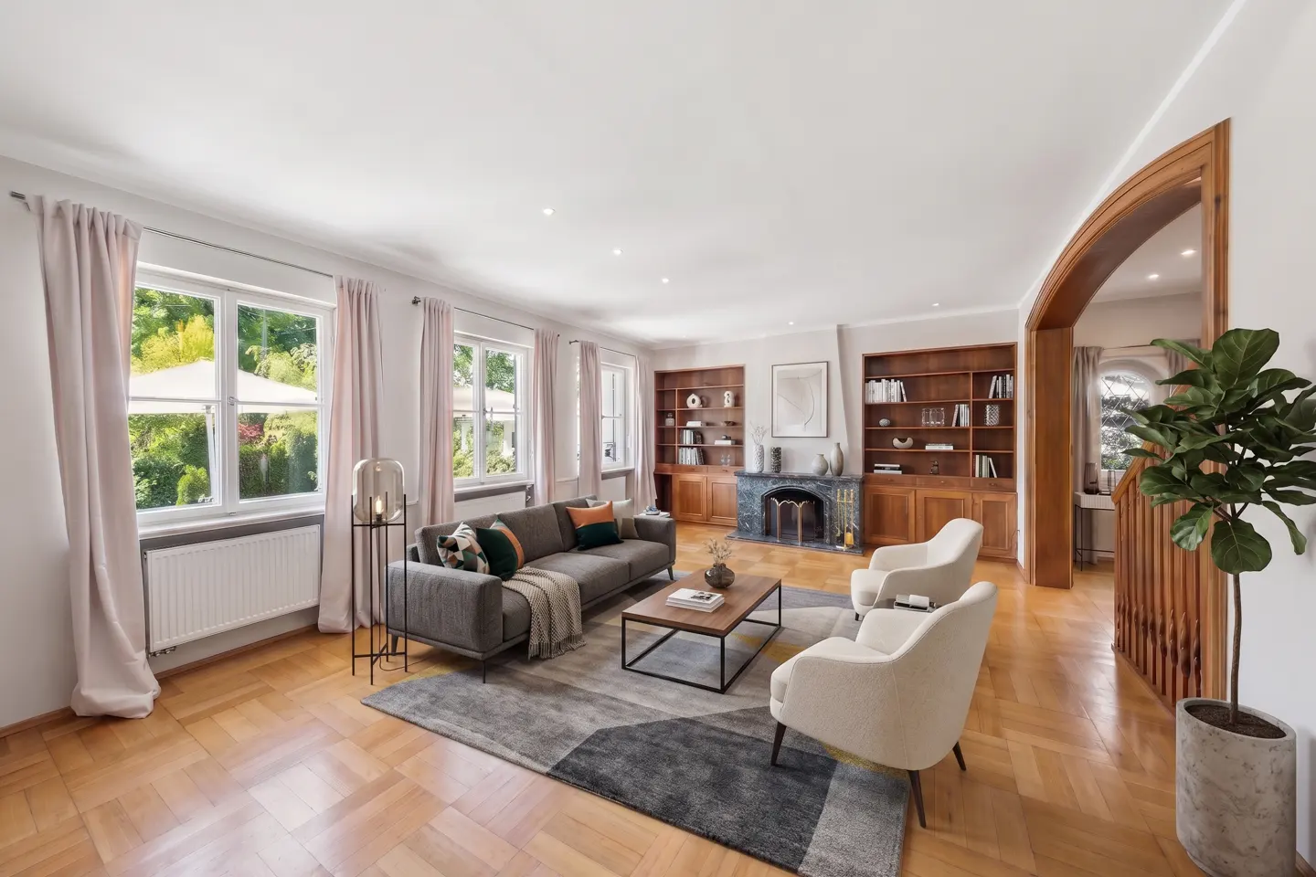 Bright living room with hardwood floors, gray sofa, two white armchairs, and built-in bookshelves flanking a fireplace.