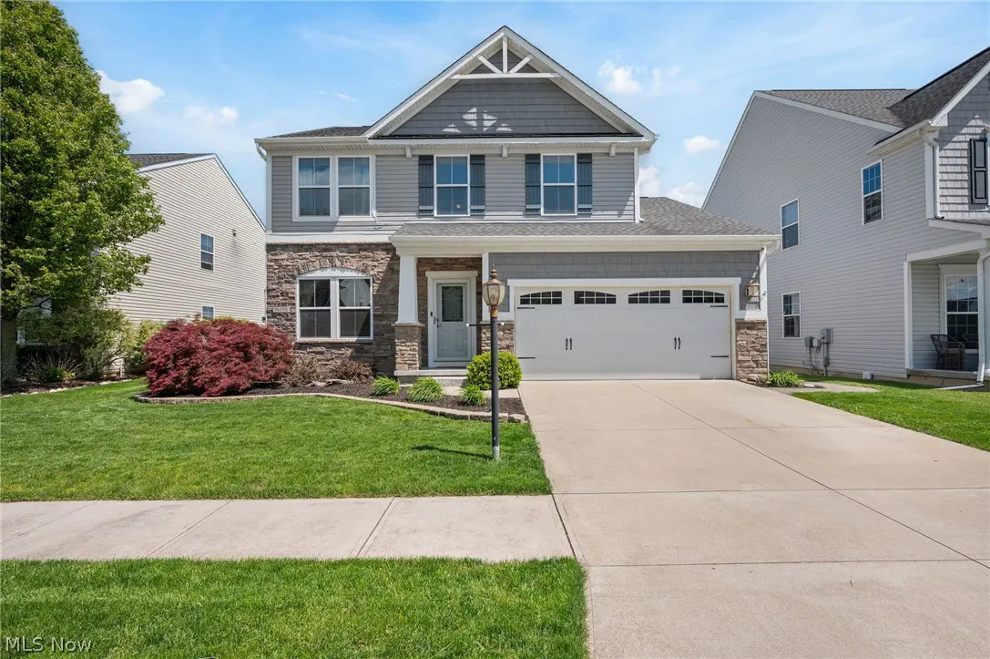 Two-story house with gray siding, stone accents, white trim, and a two-car garage on a sunny day.