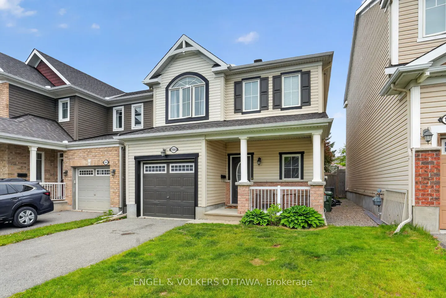 Two-story beige house with a dark gray garage door, white trim, and a green lawn under a blue sky.