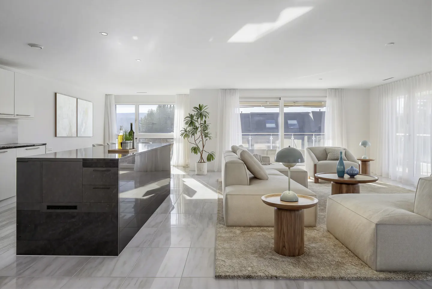 Modern open-plan living area with a dark kitchen island, beige sectional sofa, and large windows with sheer white curtains.