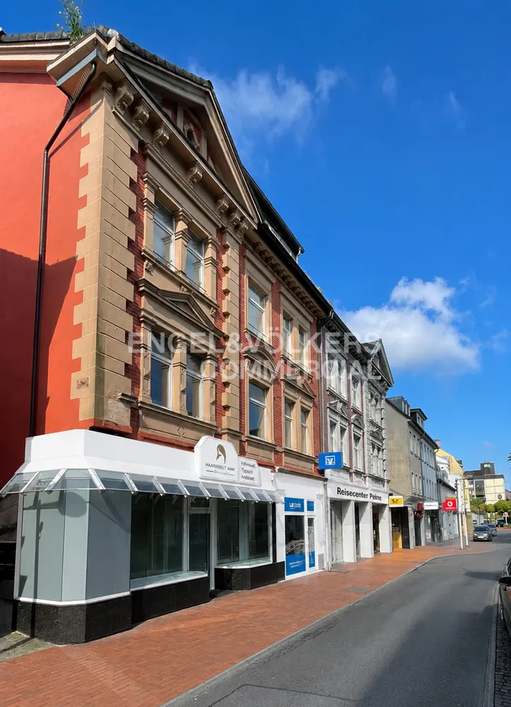 Street view of multi-story commercial buildings with storefronts under a blue sky.