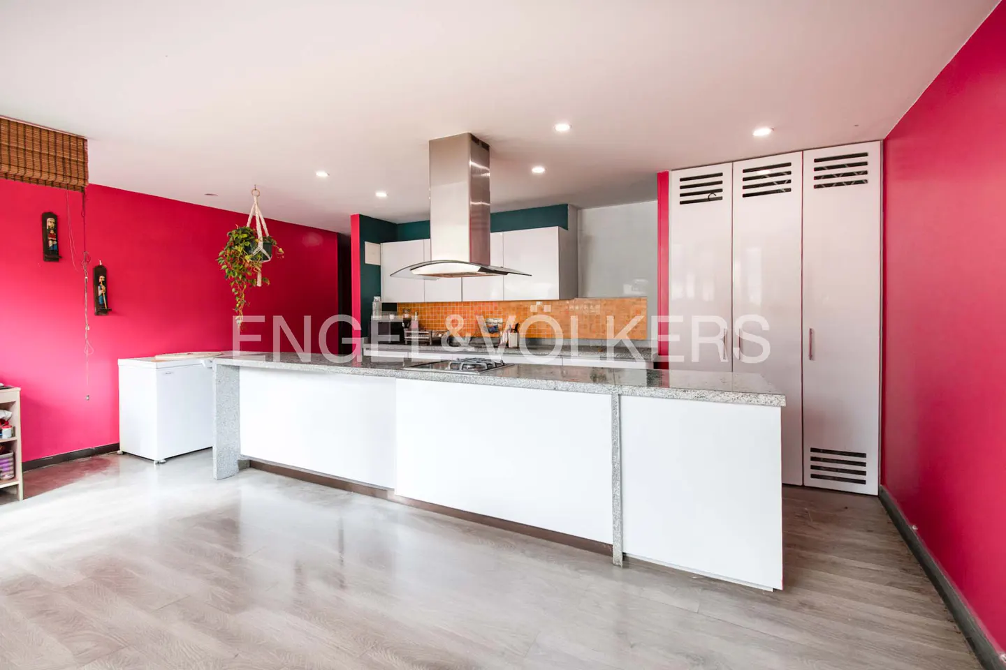 Bright kitchen with pink walls, white cabinets, and a large island with a granite countertop. Stainless steel range hood above the stove.